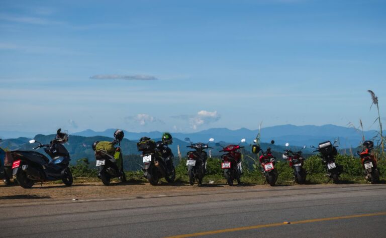Row of motorbikes in Chiang Mai Province parked on the side of the road with beautiful mountain views and blue sky in the background. Doi Kio Lom viewpoint along the Mae Hong Son Loop.