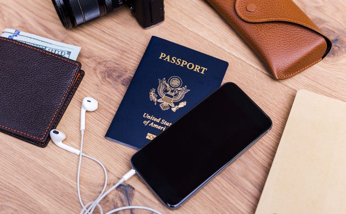 Traveling concept with travel items and blank cell phone on wooden desktop.