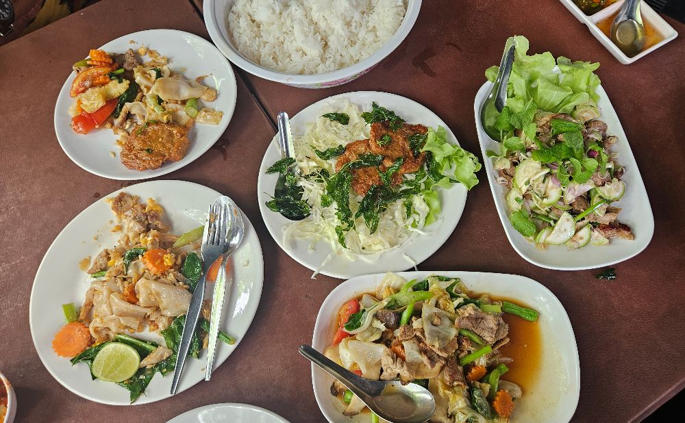 table of thai food, noodles, fish cakes, larb moo, stir fry